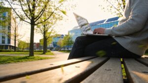 A peaceful public park landscape featuring a professional working remotely on a laptop with modern infrastructure in the distance.