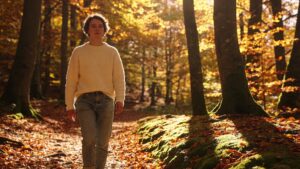A person walking alone through a sunlit forest path without their phone, representing deliberate nature time as a resilience-building strategy in an uncertain world.