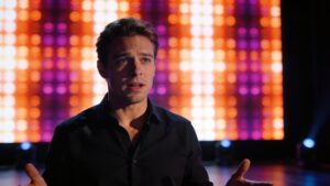 An actor illuminated naturally by the ambient light reflecting from a colorful digital backdrop panel.