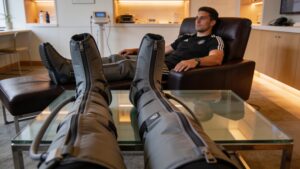 An athlete utilizing automated pneumatic compression sleeves on their legs within a premium recovery studio.