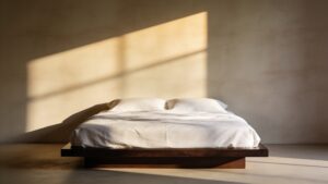 An elegant, minimalist bedroom featuring crisp white linen bedding and soft morning sunlight casting shadows on the wall.
