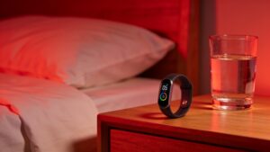 A minimalist bedroom nightstand with a fitness tracking ring resting under warm red ambient lighting.