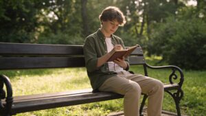 Young man lying on grass in a park journaling in a notebook during a mindfulness exercise.