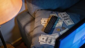 "Money and a TV remote on a couch, representing rising streaming subscription costs"