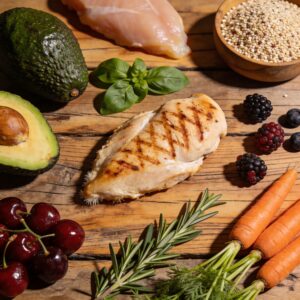 Overhead arrangement of unrefined whole produce, fresh berries, and clean proteins on wood.