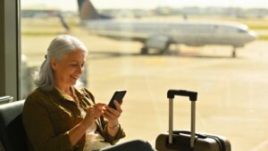 Older traveler checking her phone at an airport window before a trip"