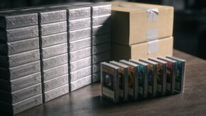 Large stack of unopened card packs next to a small row of carefully sleeved cards, representing oversupply risk"