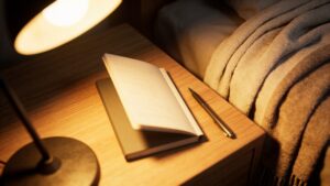 Notebook and pen on a bedside table under a dim lamp.